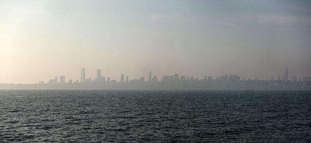 The misty cityscape of Mumbai's skyscrapers in front of the sea viewed from Marine Drive during the sunset