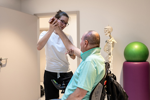 A physiotherapist examines a patient in a wheelchair. A physiotherapist does rehabilitation exercises with a disabled person and a therapy table.