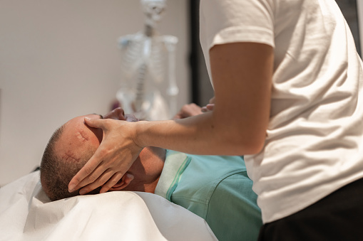 A physiotherapist examines a patient in a wheelchair. The patient is lying on the therapy table at the doctor. The doctor examines his injury and the healing of the wound and stitches, as well as the condition after the operation. The doctor examines the healing of stitches after skull or brain surgery.