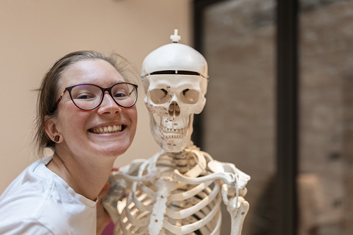 Funny, fun. A model of the human skeleton in the background during orthopedic rehabilitation of a disabled person.
Physiotherapist poses with a skeleton model and plays pranks.
