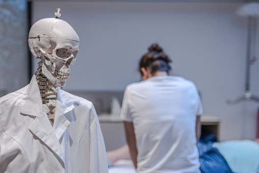 A physiotherapist does rehabilitation exercises with a disabled person on the therapy table.Funny, fun. A model of the human skeleton in the background during orthopedic rehabilitation of a disabled person.