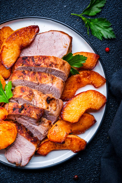 istock Baked pork tenderloin with spicy caramelized apples on plate, black table background, top view 2125012507