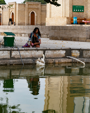Lady sitting by a lake looking at a swan in Chor Bakar, sittingon a window in Uzbekistan