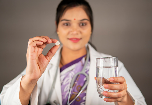 Portrait of indian female doctor vitamin pill and glass of water in hand and looking at the camera with a smile.