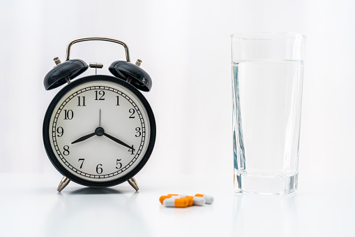 Pills, capsules and alarm clock on white background