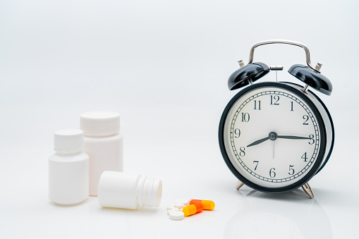 Pills, capsules and alarm clock on white background