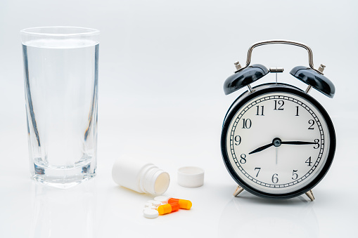 Pills, capsules and alarm clock on white background