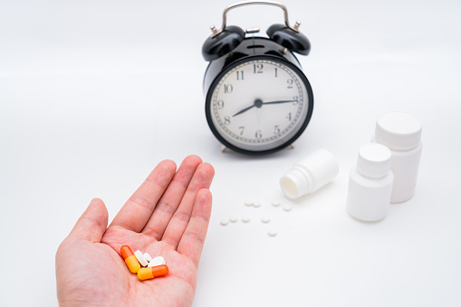Medicine bottles, alarm clocks, and pills in hand against a white background