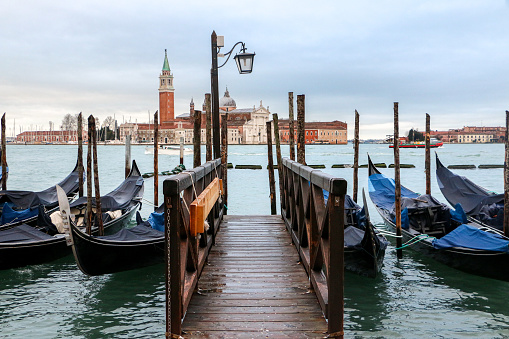 Picturesque view of Venice, gondolas docked at Riva degli Schiavoni, wooden walkway leading to view of the iconic Church of San Giorgio Maggiore in the background - Venice, Italy