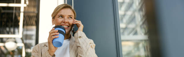 istock Female entrepreneur talking phone while drinking coffee standing on office building background 2125165338