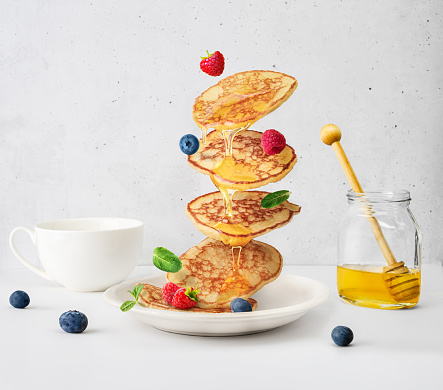 Flying pancakes with honey and berries over white table