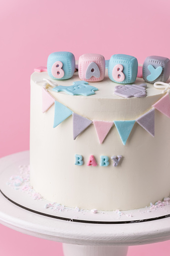 Baby shower party cake with white chocolate frosting. Guess the gender of the upcoming child. He or She cake. Reveal the gender of the unborn baby. Blue or pink sponge bisquit inside. Pink background