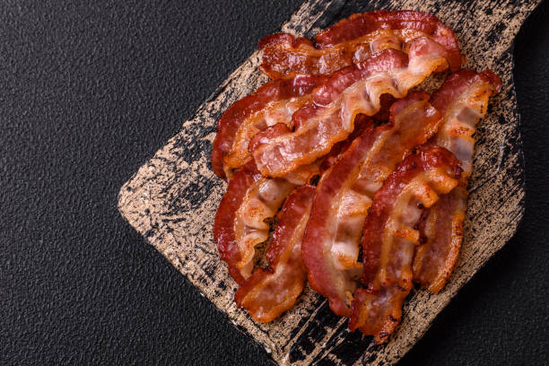Delicious fresh fried bacon with salt and spices on a dark background as an ingredient for preparing a hearty breakfast
