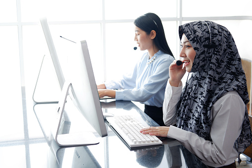 Smiling Asian and Muslim women is call center or secretary operator is wearing a headset and a microphone for consultant to customers. Technician Support staff for help resolve technical issues