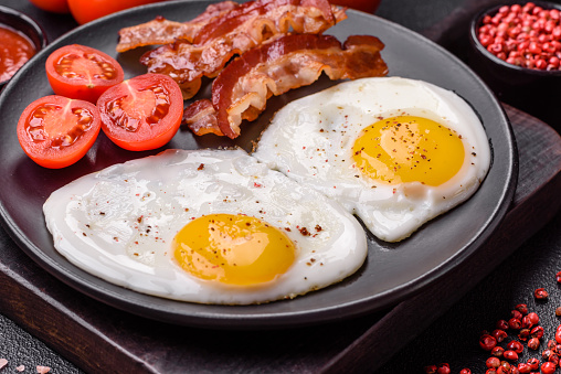 English breakfast with fried eggs, bacon, beans, tomatoes, spices and herbs. A hearty and nutritious start of the day