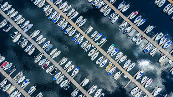 Aerial top down view of boats docking at marina, docks creating diagonal lines, with clouds reflecting on water river, Nepean Sailing Club, Ottawa, Ontario, Canada. Photo taken by drone in July 2021.