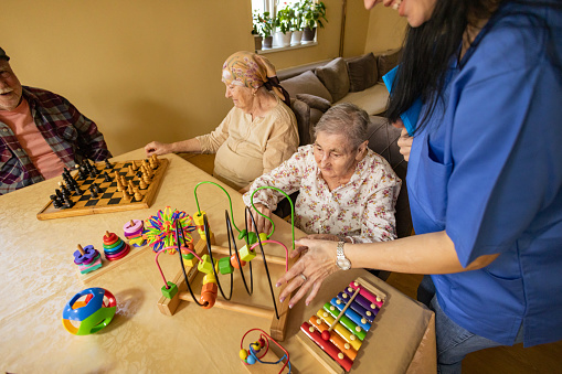 A group of seniors smiles as they playfully arrange and rearrange colorful toys on a tabletop, exercising their memory skills.