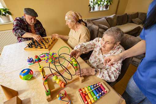 Grandparents enjoy mental stimulation through a game of chess while their nurse provides assistance and supervision.