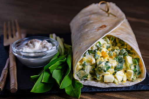Homemade burrito wraps with boiled eggs, potato, green wild garlic and sour cream for healthy breakfast on plate, close up