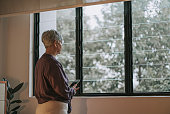 sad asian senior woman standing in front of the window looking