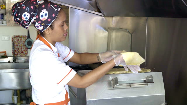 Latin woman is inside the kitchen of a small empanada food business