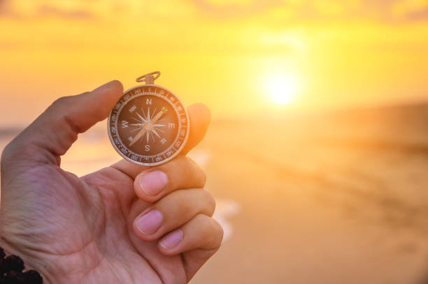 primer plano de la mano de un hombre sosteniendo una brújula magnética contra el fondo de la puesta de sol y mar. - compass exploration the way forward beach fotografías e imágenes de stock