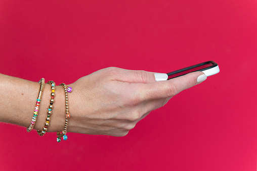 Woman's hand holding a cell phone against a magenta background