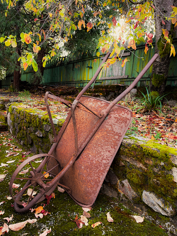A rusty metal wheelbarrow resting against a stone wall