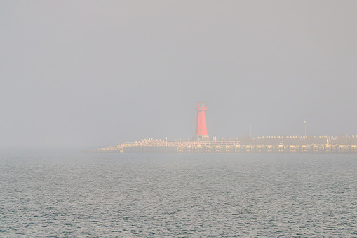 The Port of Gdansk in the fog, a lighthouse in the foreground. Baltic Sea, Gdansk, Poland