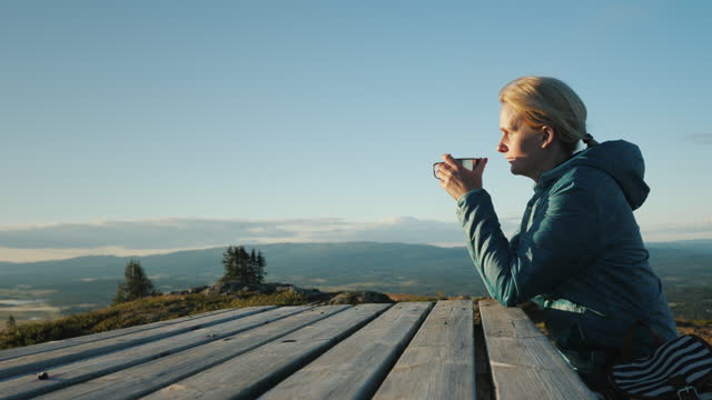 A woman traveler sits at a table high in the mountains, drinking tea. Far from civilization