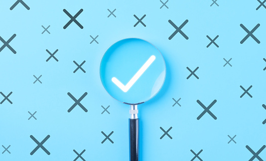 A magnifying glass emphasizing a white check mark among crossed out icons on a blue background. Quality control and approval, Checkmark to approve and Wrong mark, business project proposal or document