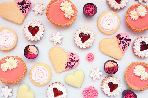 Mothers Day or love themed baking background with assorted cookies and sweet treats. Top view on a white marble background.