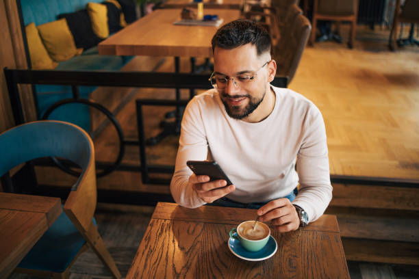 istock Young man sitting in cafeteria and using smartphone to talk with friends. 2125431048