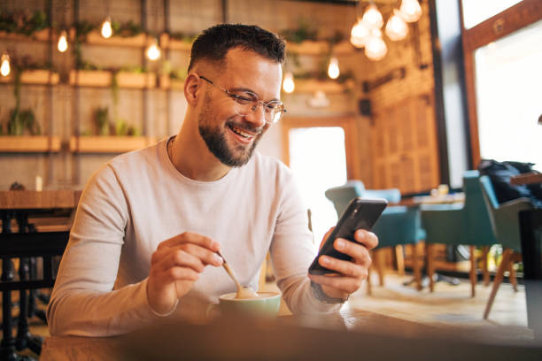 istock Young man sitting in cafeteria and using smartphone to talk with friends. 2125433639