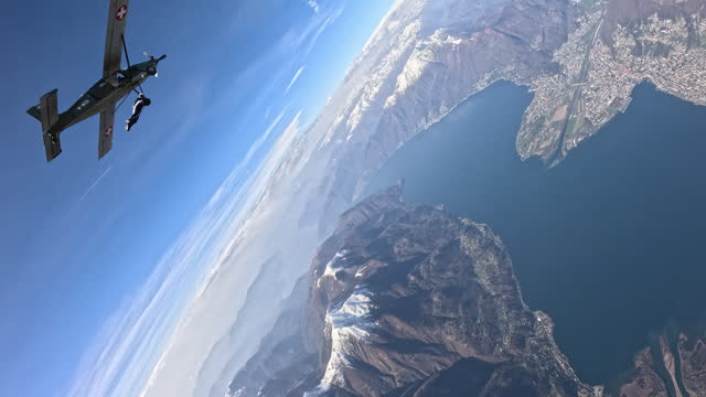 Wing suit flier leaves plane to soar above mountain landscape