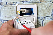 Connecting wires to wall thermostat for floor heating system, an electrician uses crosshead screwdriver for installation.