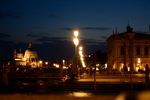 The embankment of the night ancient city in Italy is illuminated with lanterns. Ancient architecture of the old town in the background
