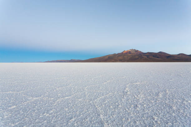 Endless white salt flats stretching into the horizon. Cloud-dotted blue sky above a serene landscape. Tranquil and natural scene of wide-open spaces.