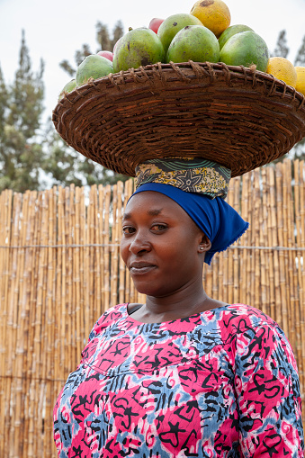 Portrait of a young African woman with headscarf and a basket with fruit on her head. Rwanda