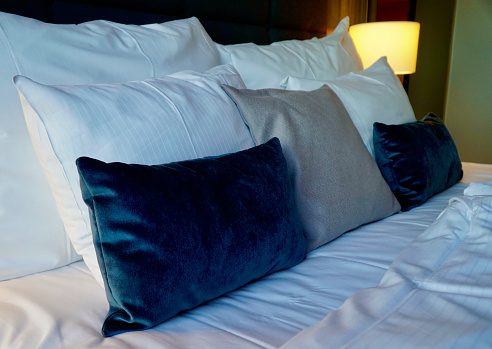 Hotel room bed with white linen and elegant blue pillows.