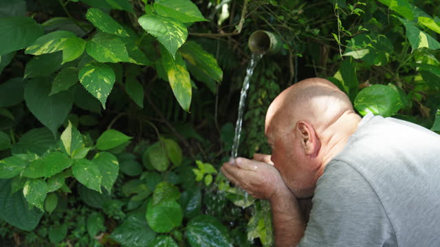 SLO MO Shot of Man Drinking Flowing Water from Pipe in Cupped Hands at Forest During Hike. A Natural Source of Clean Drinking Water.