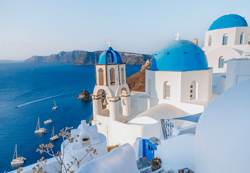 The panoramic view of the old town of Oia or Ia on the island of Santorini, Greece, features, white washed houses, blue dome churches, hotels and traditional windmills. The picturesque landscape captures the beauty of the after-sunrise in la Village, a famous spot on the Greek island of Santorini town. The colorful buildings on the cliffside add to the picturesque atmosphere in Cyclades, Greece. Scenic travel background for romantic vacations and honeymoon holidays.