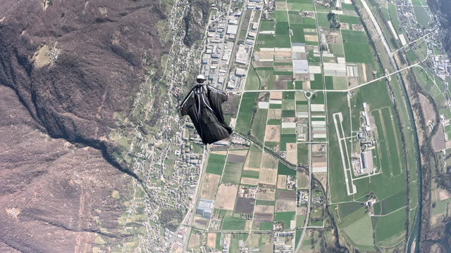 Wing suit flier soars above mountain landscape