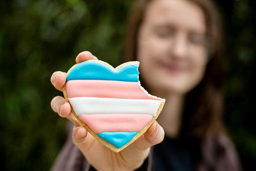 This portrait is a celebration for Trans Day of Visibility, a transgender teen savors a moment of joy, indulging in heart-shaped cookies intricately decorated with the vibrant hues of the trans flag. Each bite is a sweet affirmation of identity, a testament to resilience and pride.