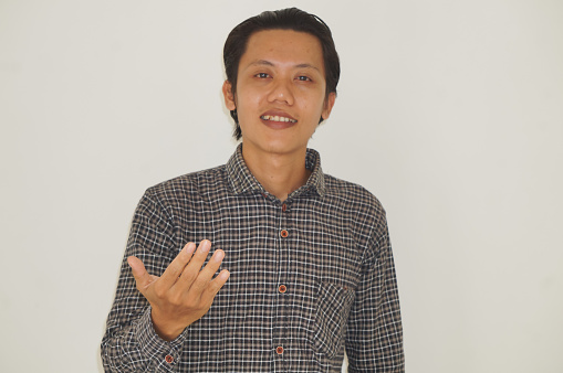 Young Asian man standing and smiling with inviting hand gesture