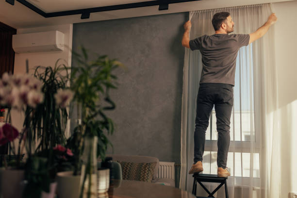 istock Man hanging curtains in bright living room 2125914176