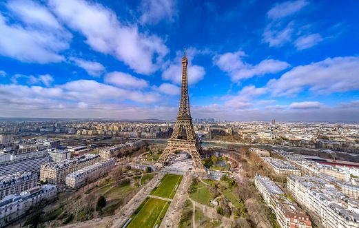 June 9, 2018 - Paris, France. A wide angle view of the Eiffel tower in Paris on a blue sky day with people walking through the park.