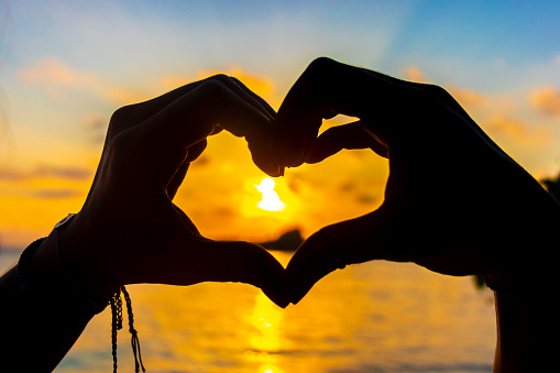 Heart made of hands with turquoise water and amazing golden colorful sunset on Rasdhoo Atoll Maldives.
