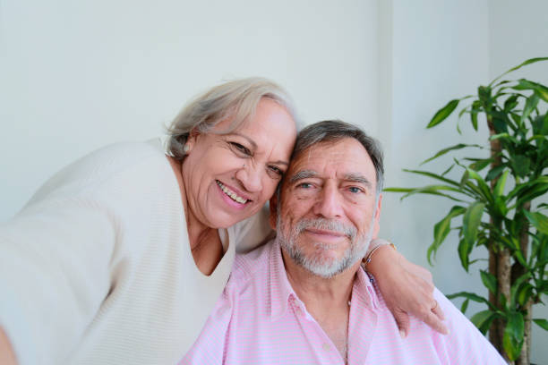 istock Older couple smiles while take a selfie with cell phone sitting at home 2125975214