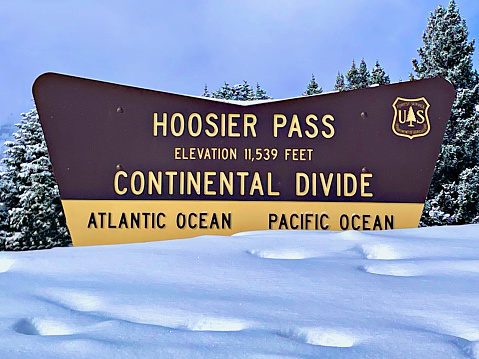 Breckenridge, Colorado, USA - February 10, 2024: The Hoosier Pass sign surrounded by deep snow and snow-covered pine trees in the background.